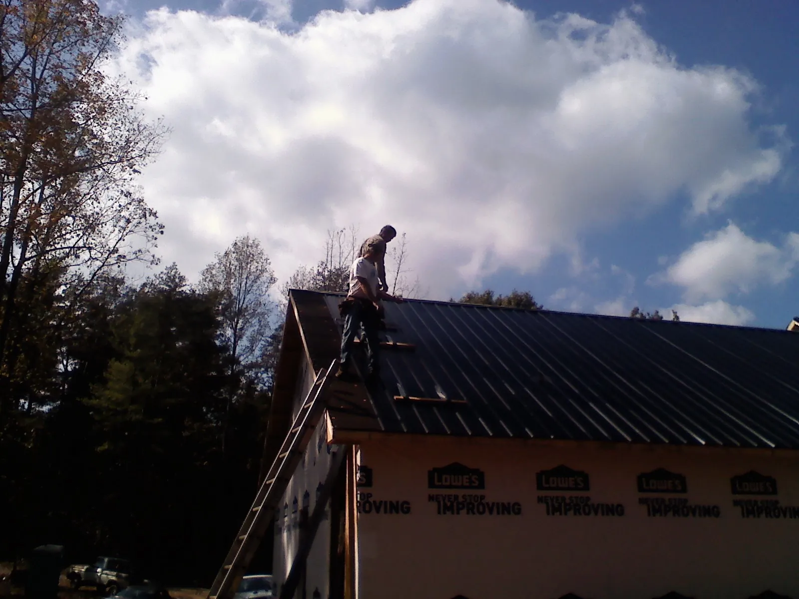 Roofer fastening dark metal panels high against a cloudy sky, from a Roof Inspection job in Apache Junction